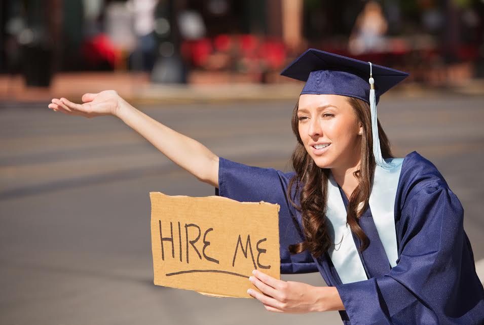 Single college graduate in gown holding hire me sign